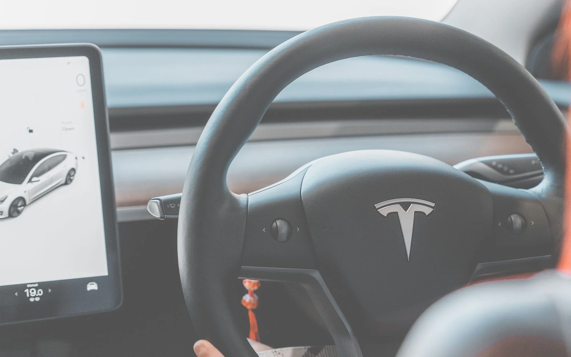 Steering wheel and touchscreen of a right-hand-drive Tesla Model 3, with the car shown on the screen