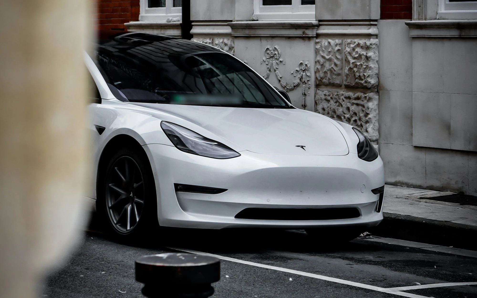Front of a white Tesla Model 3 parked in a marked bay beside a stone-fronted building on a street in Worcester